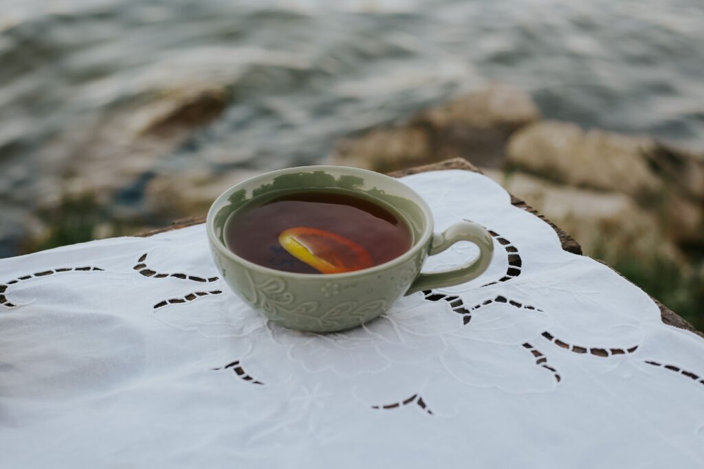A ceramic cup of tea with a lemon slice, elegantly placed on a lace cloth by a serene lakeside.